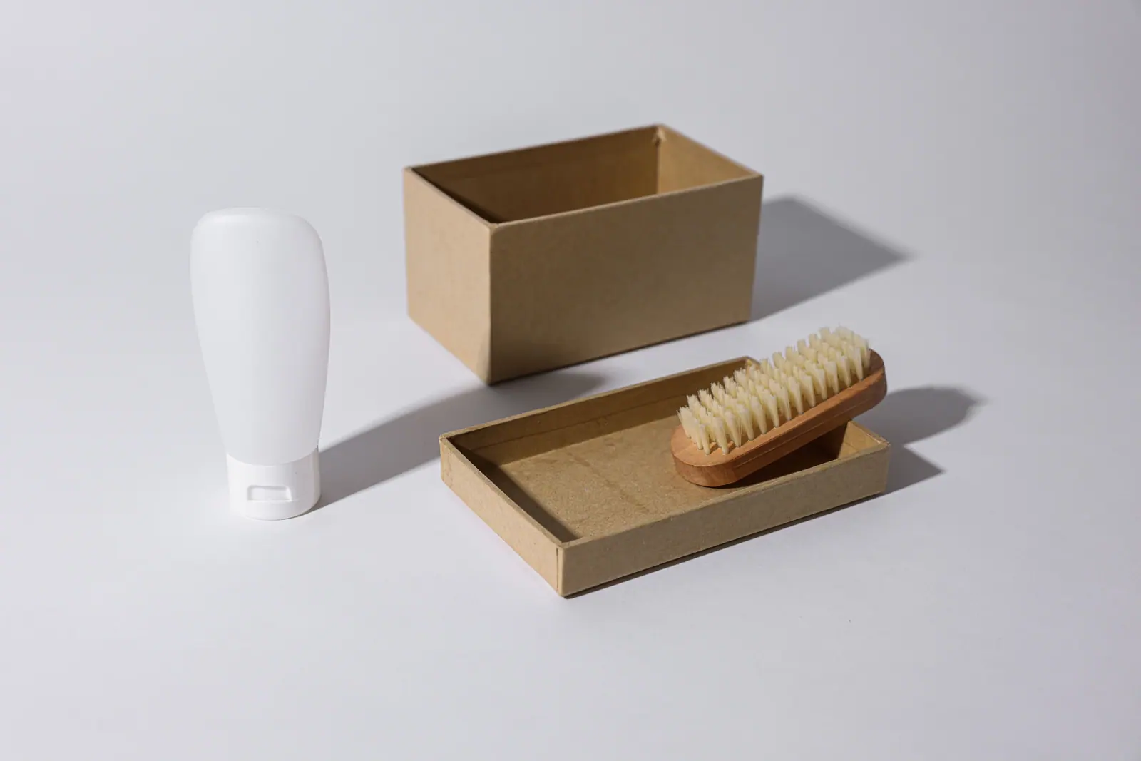 A white bottle beside an open kraft box holding a natural-bristle brush.