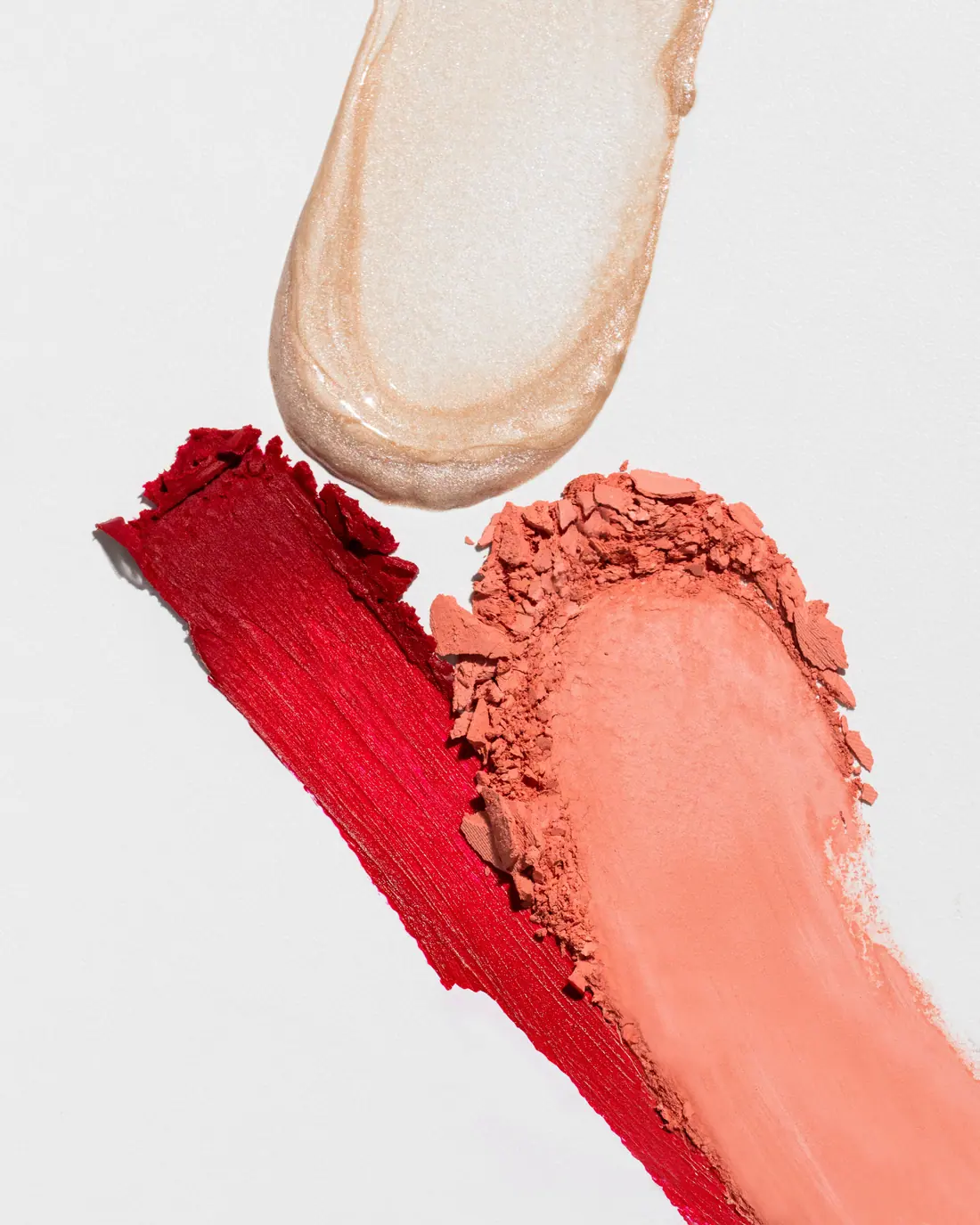 Swatches of highlighter, red lip colour and coral blush on white.